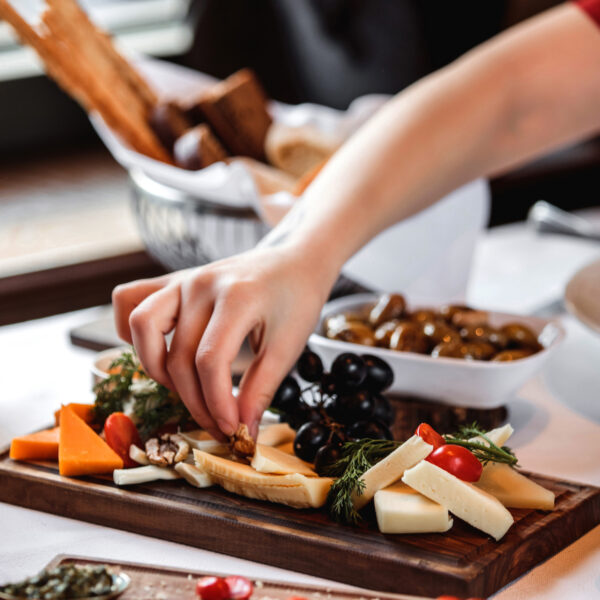 sidce view of various types of cheese with nuts grapes and honey on a wooden platter